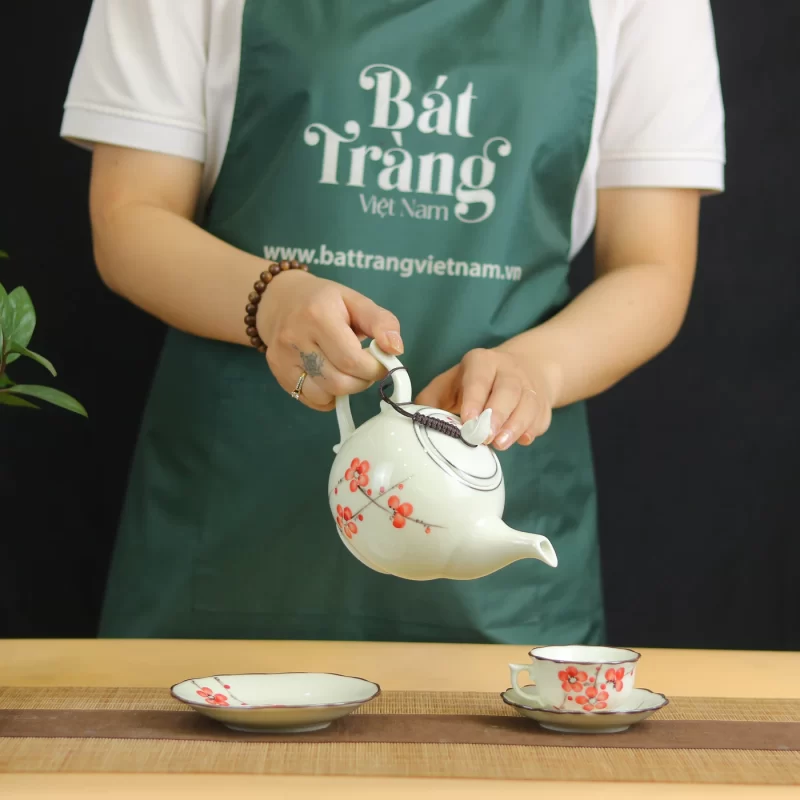 Ảnh chụp góc cầm nghiêng ấm hoa đỏ cùng chén và đĩa kê